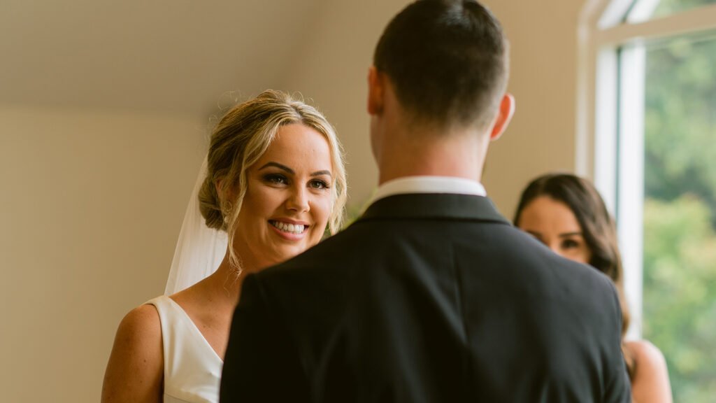A bride smiles as her husband says his wedding vows to her during their wedding ceremony.