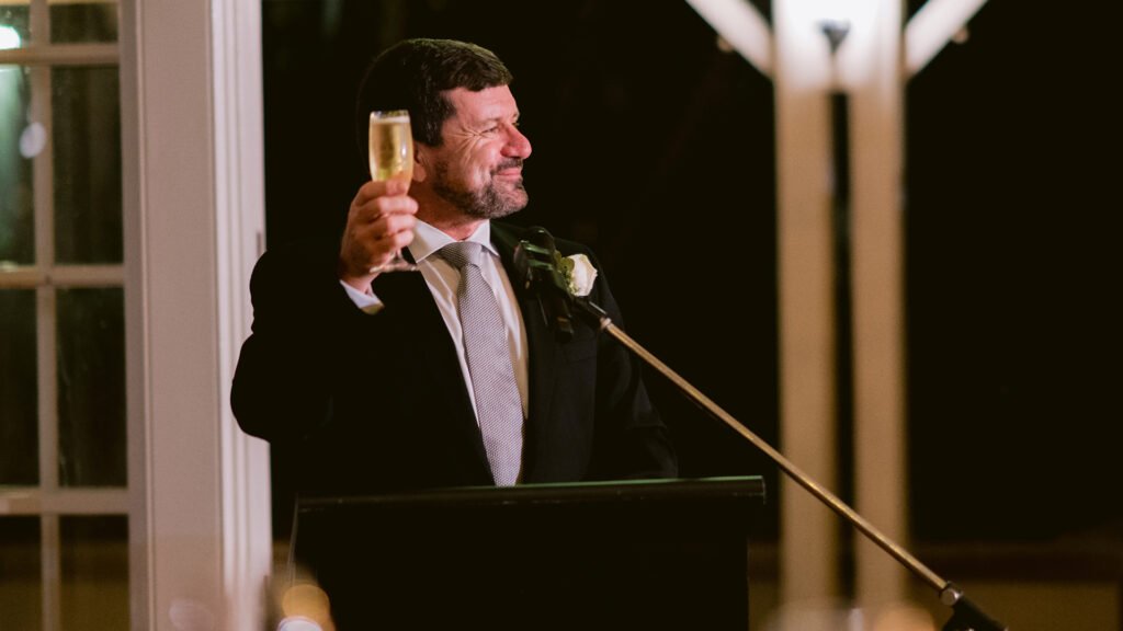 The father of the bride toasts the bride and groom at their wedding reception after giving his speech.