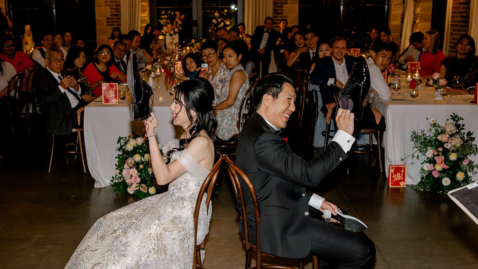 A bride and groom laugh and raise their shoes while answering questions during the wedding shoe game.