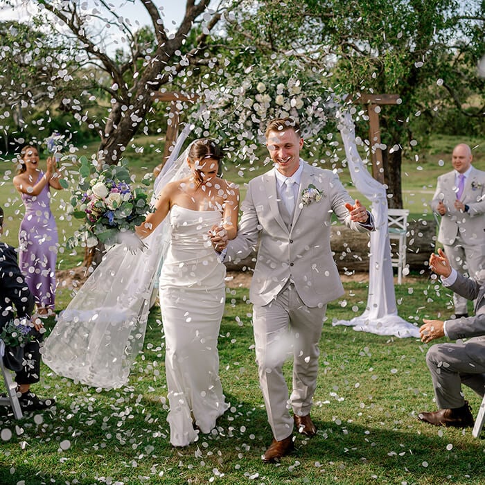 A bride and groom walking out of their ceremony to a shower of confetti.